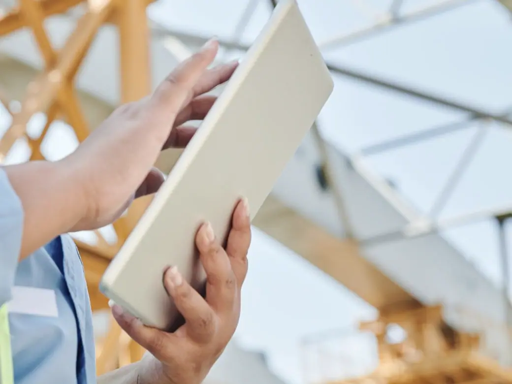 Hands holding a tablet on a job site, with steel framing behind.